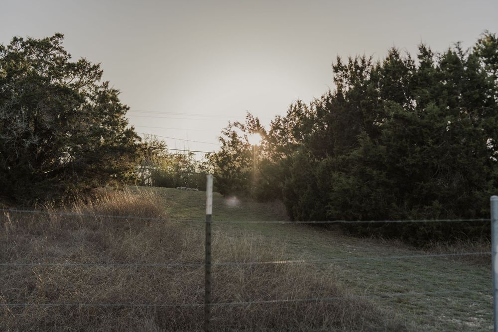 A wooden cross marker stands on a trail at sunset with trees in the background.