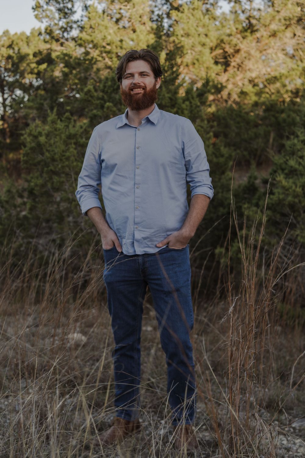 A person in casual attire stands on a nature trail surrounded by tall grass and trees.