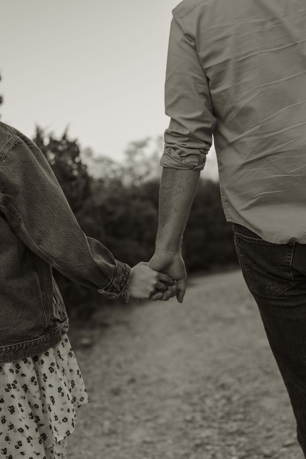 Black and white photo of two people holding hands while walking outdoors.