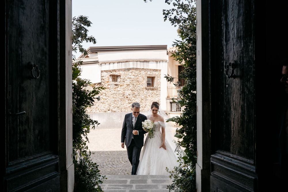 Wedding couple silhouetted in grand doorway of historic stone building during outdoor ceremony.