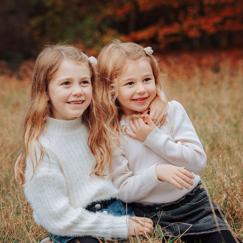 Two young sisters kneeling and cuddling in a meadow naturally laughing.