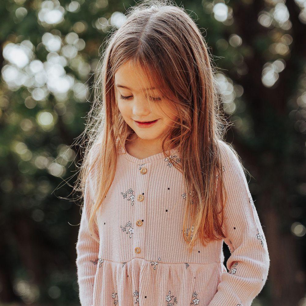 Natural photograph of a young girl looking down in a woodland smiling.