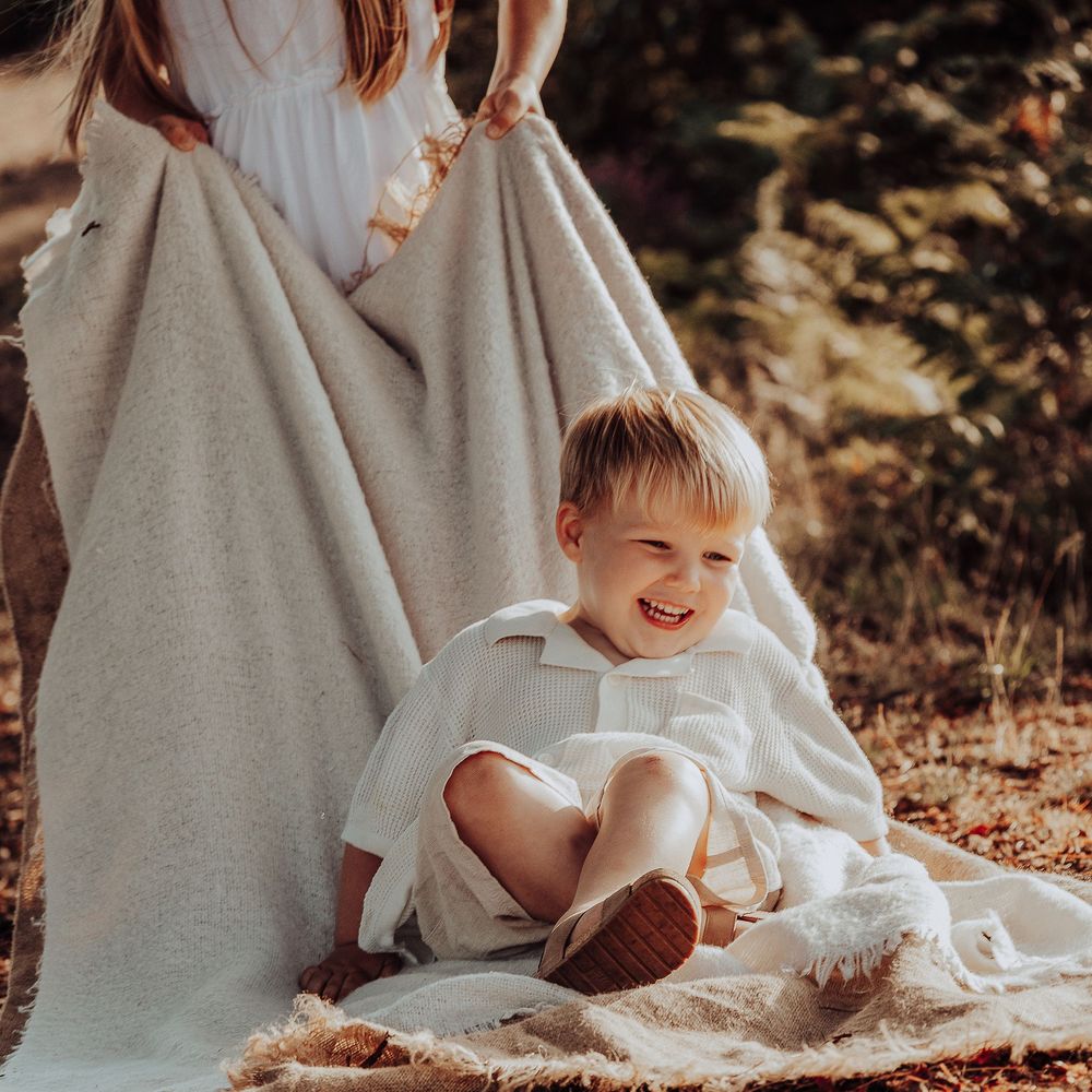 Young boy laughing whilst being pulled on a rug during a golden hour photo shoot.