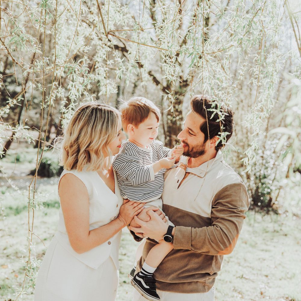 A young couple holding their little boy together laughing in a woodland setting.