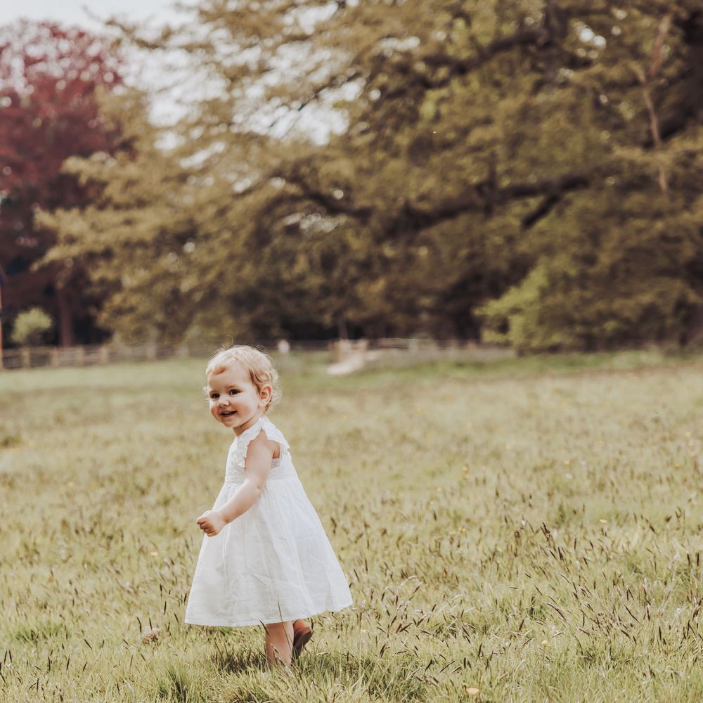 Image of a little girl toddler in a white dress taking her first steps in a field.
