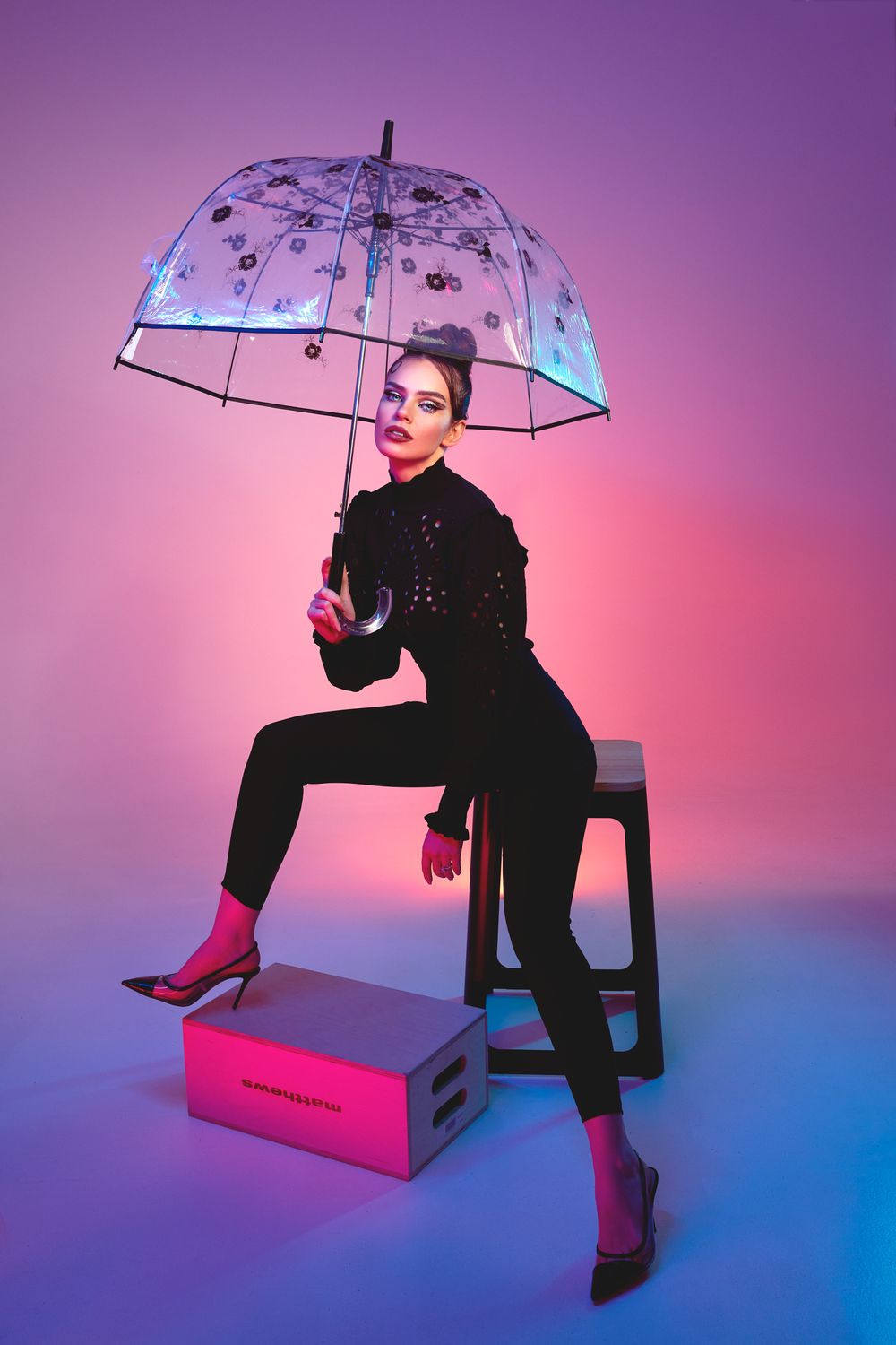 Stylish portrait with clear umbrella against gradient purple and pink background.