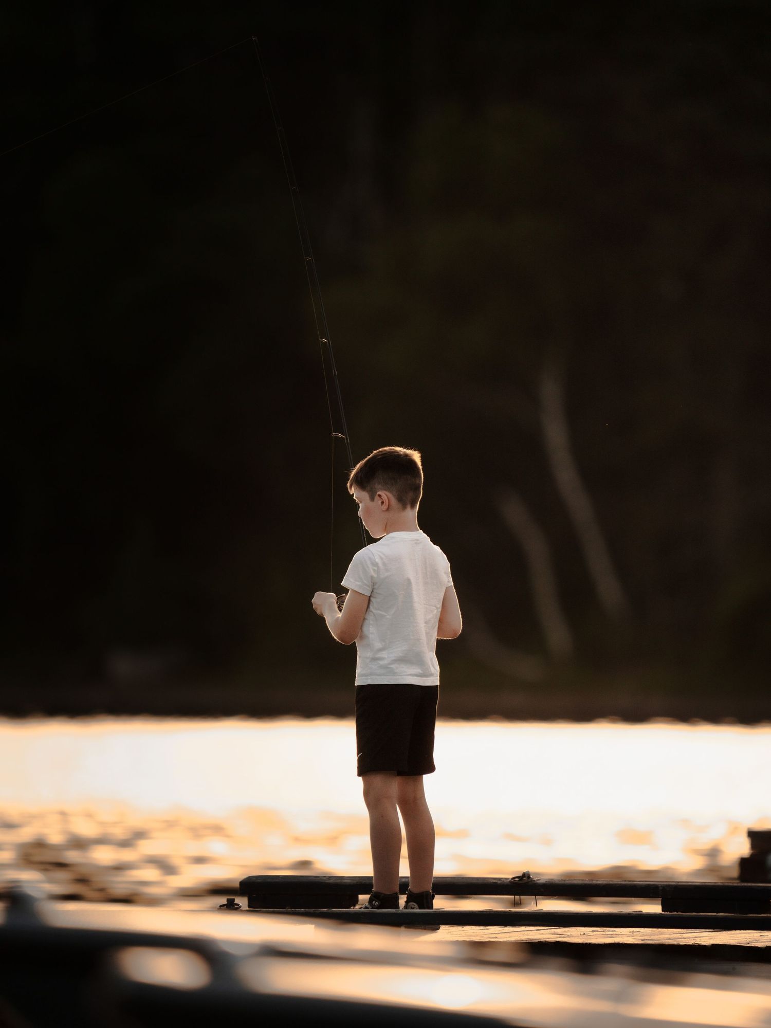 Silhouette of young angler fishing from dock during golden sunset.