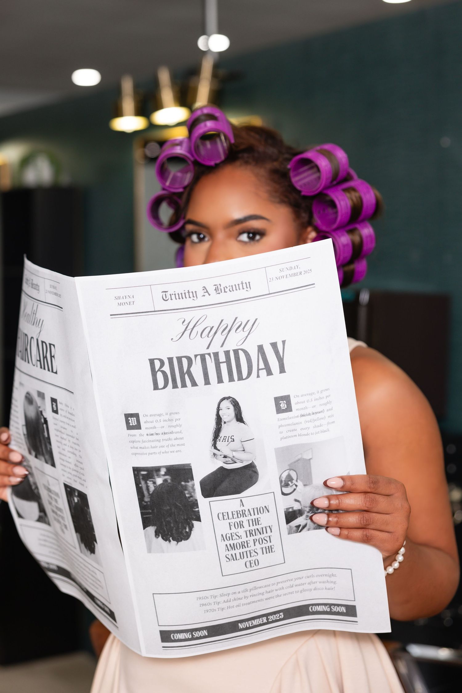 Person with purple hair rollers holds up a newspaper-style birthday announcement while getting ready.