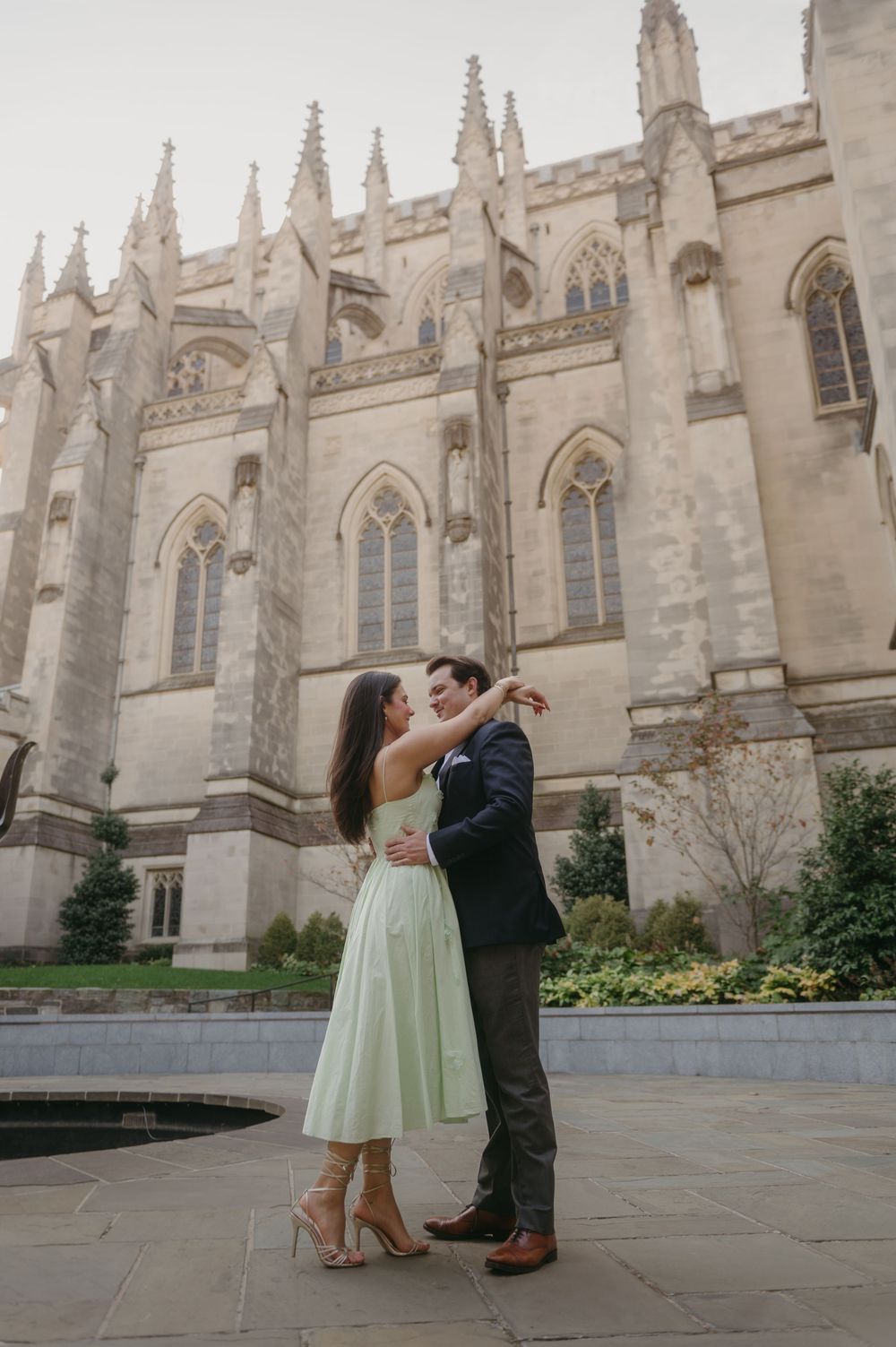 A couple dances playfully in front of a gothic cathedral's ornate stone facade.