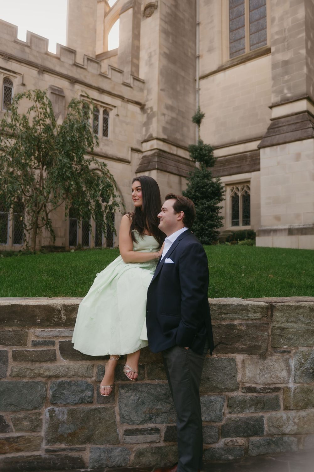 Couple poses playfully on stone wall outside Gothic church architecture on sunny day.