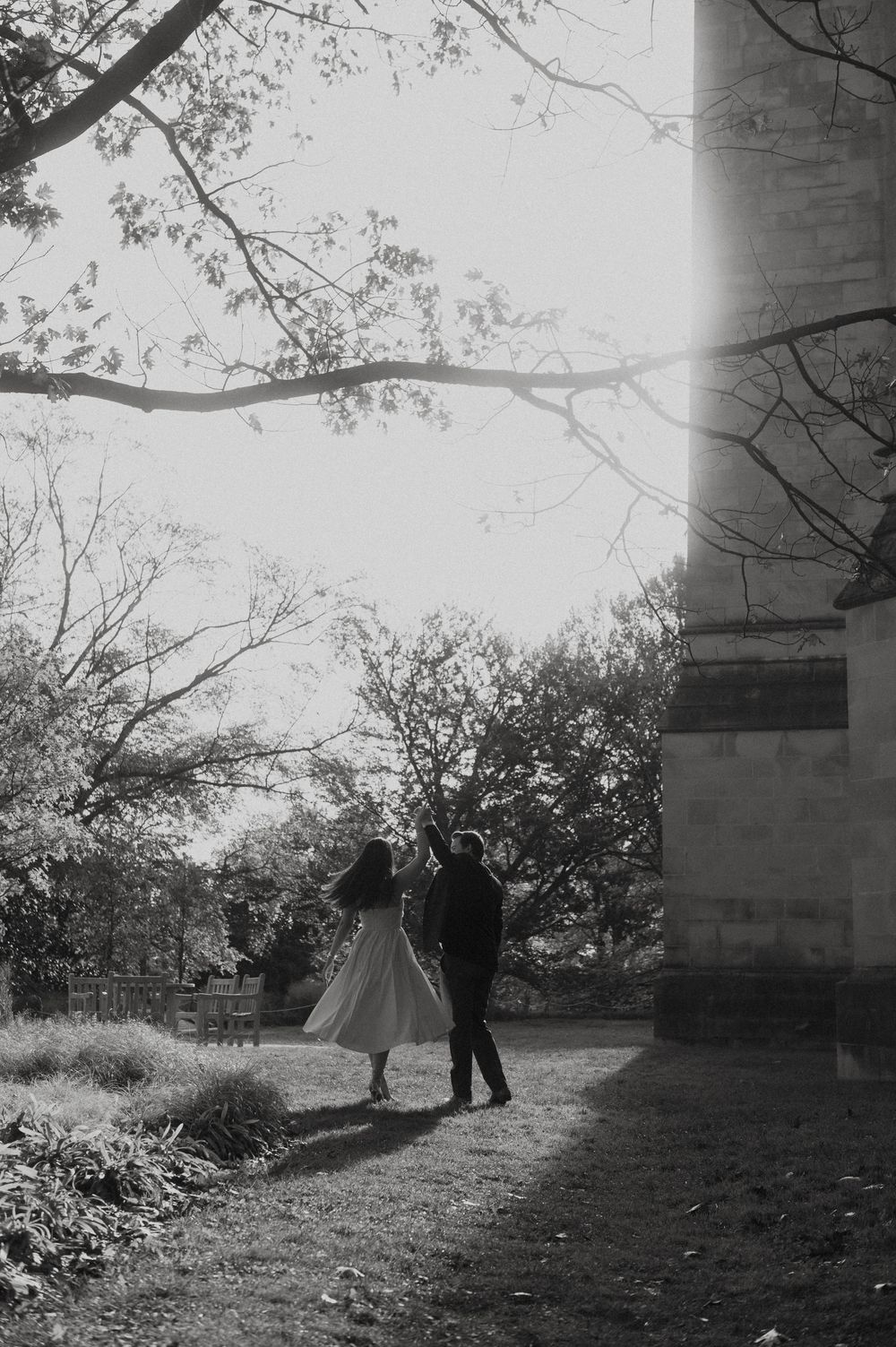 A romantic black and white silhouette of a couple dancing near a stone building surrounded by trees.