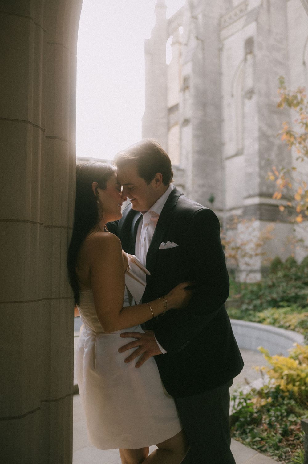 A couple shares an intimate moment under gothic stone columns at sunset.