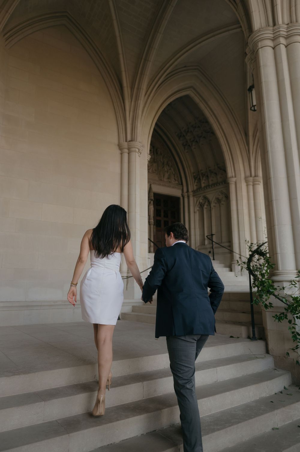 A couple walking up stone steps in an elegant archway corridor of a historic building.