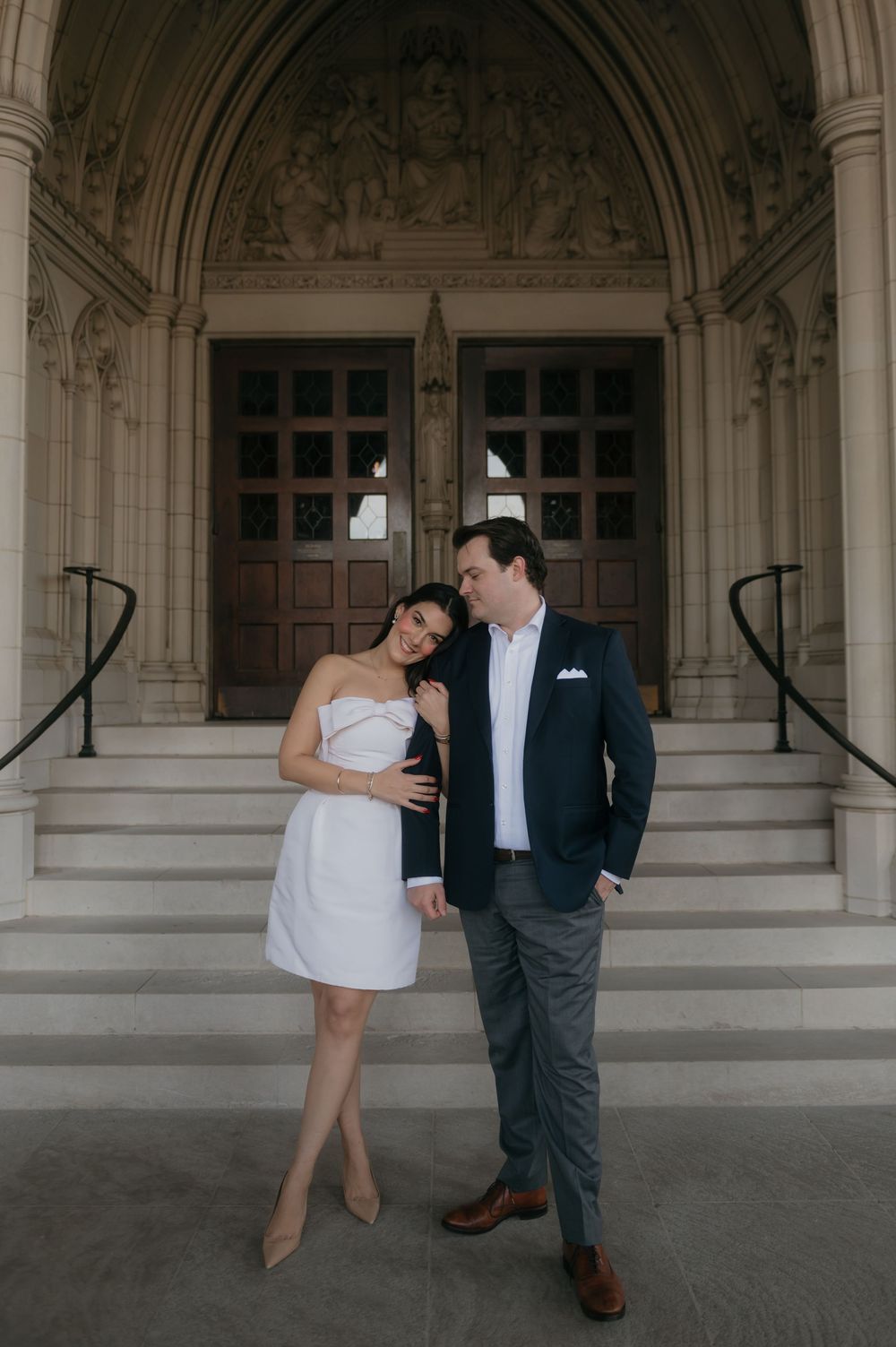 Artistic engagement photos showing couple in formal attire posing beneath ornate stone archways.