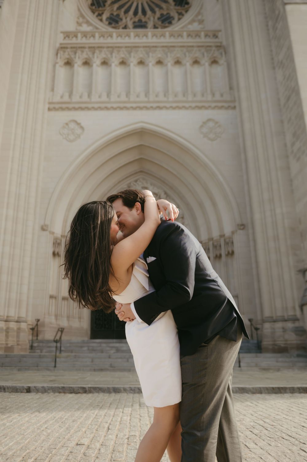 A couple embraces in front of an ornate gothic cathedral entrance with detailed stone carvings.