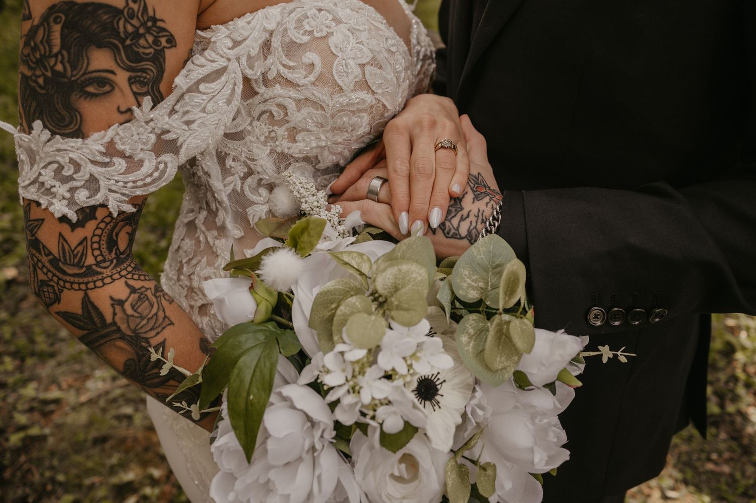 Close-up of a delicate white lace wedding dress with floral details and white bouquet in outdoor setting.
