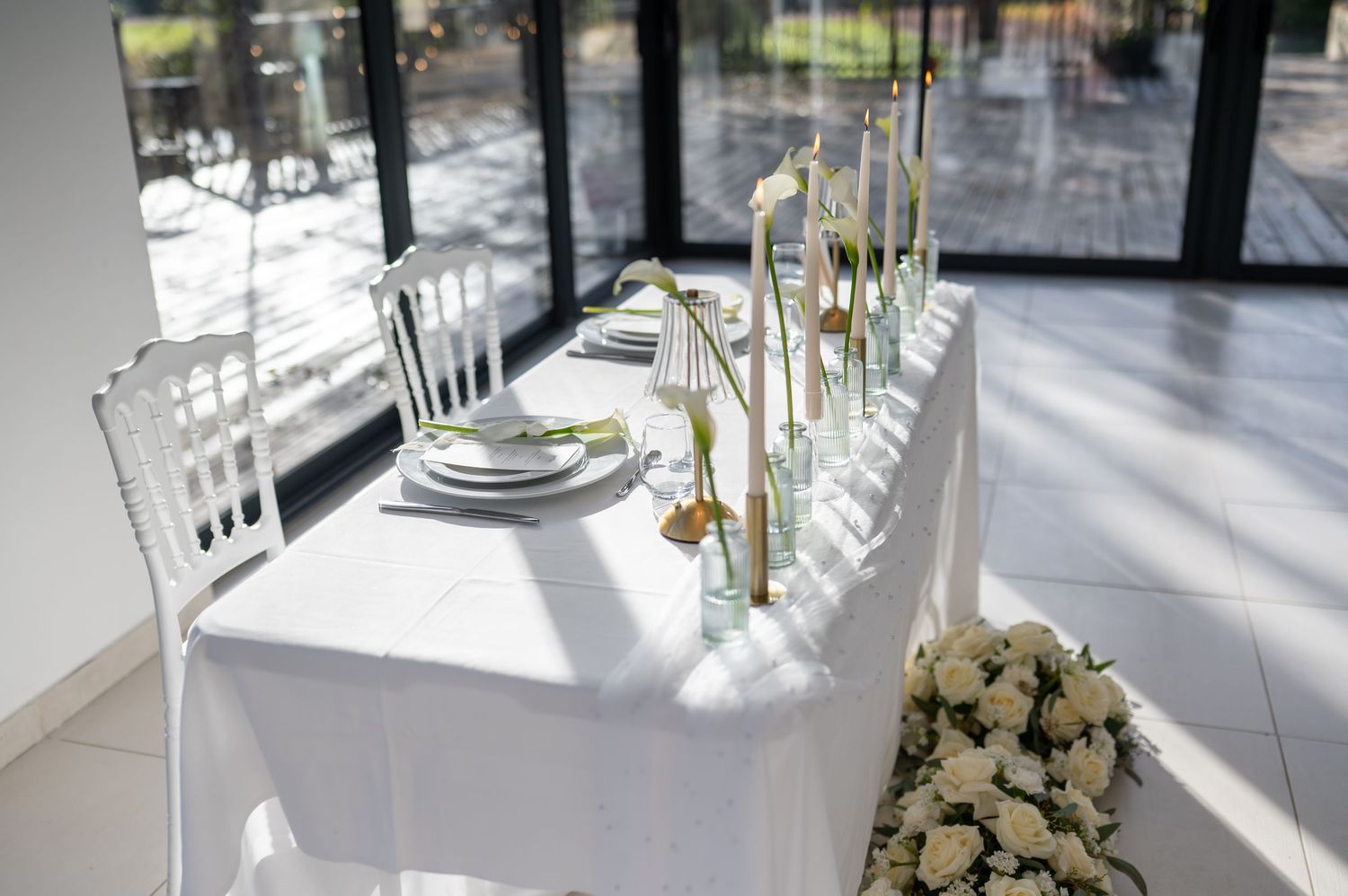 D'élégants arrangements floraux blancs dans de grands vases en verre décorent un espace événementiel moderne avec un éclairage naturel.