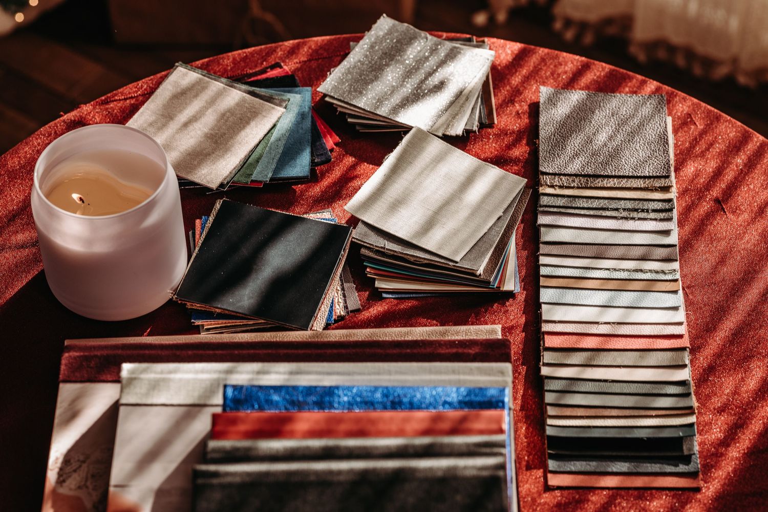 Playing cards and cloth napkins arranged on a red tablecloth next to a glass candle holder.