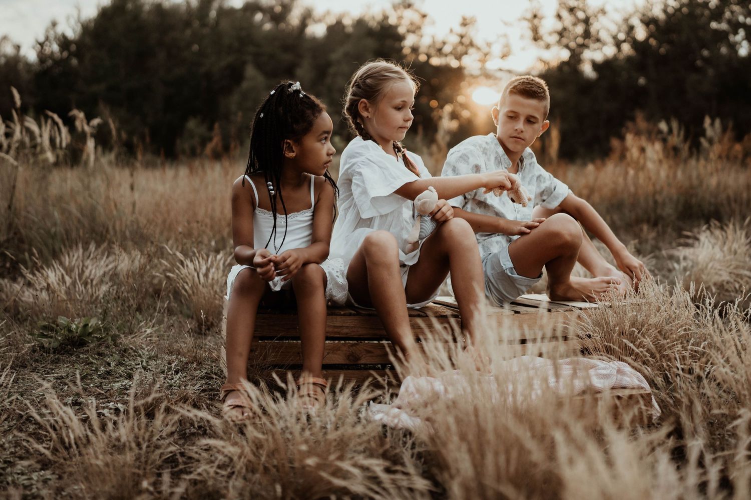 Three people sitting on wooden crates in a field during sunset.