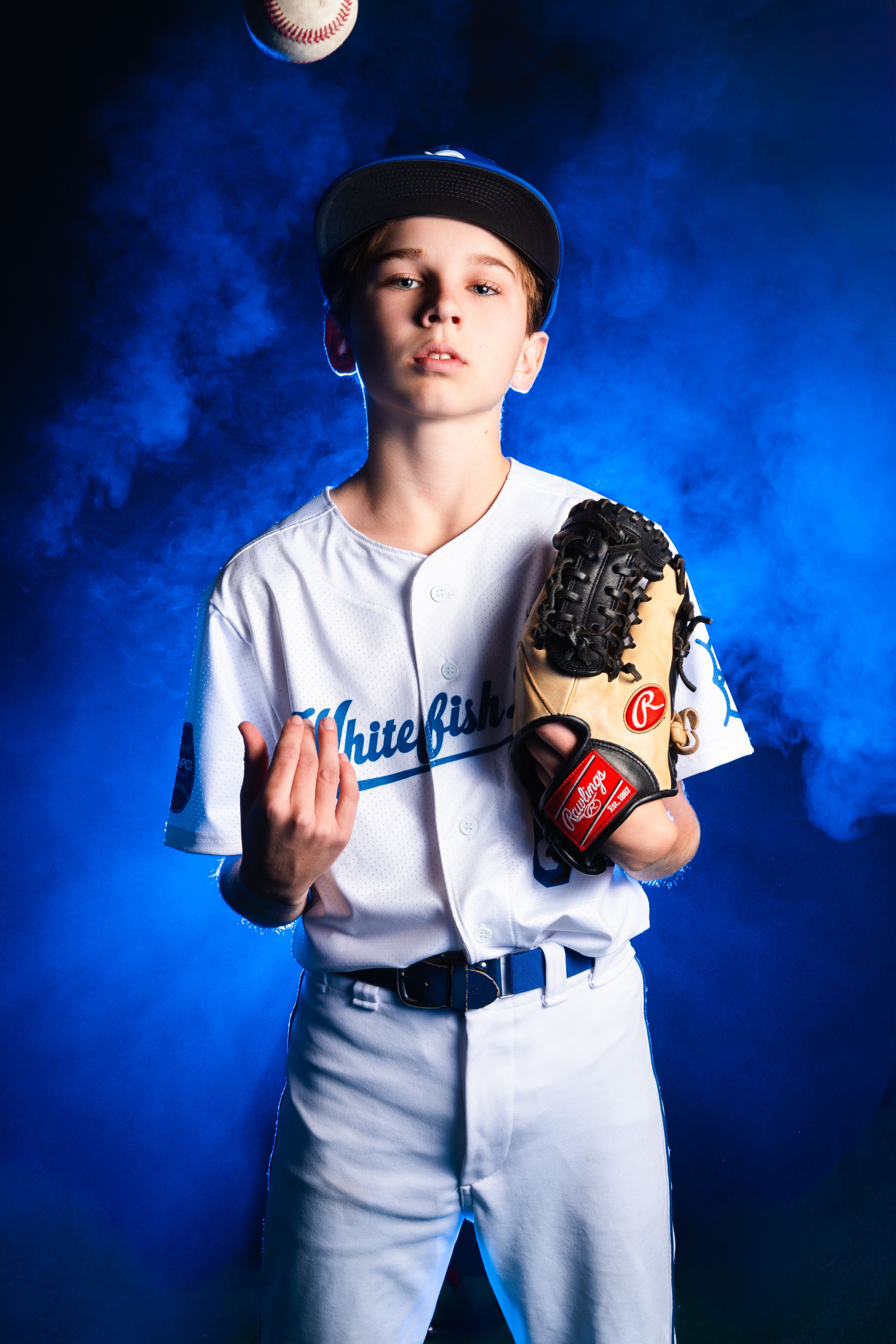 Baseball player in white uniform poses with baseball glove against blue smoky background.