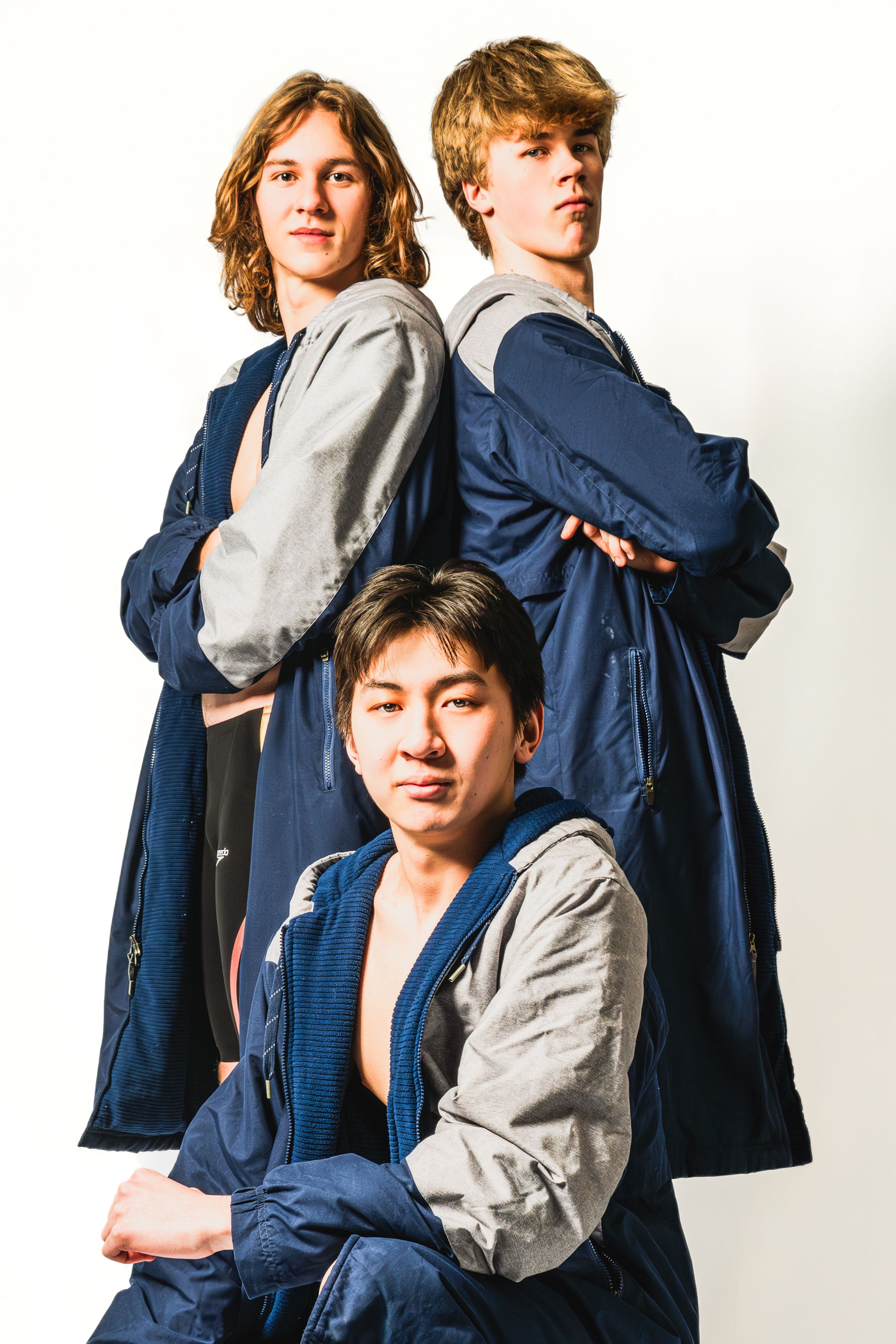 Three people pose in coordinated navy blue and gray casual outfits against a white background for a fashion photo shoot.