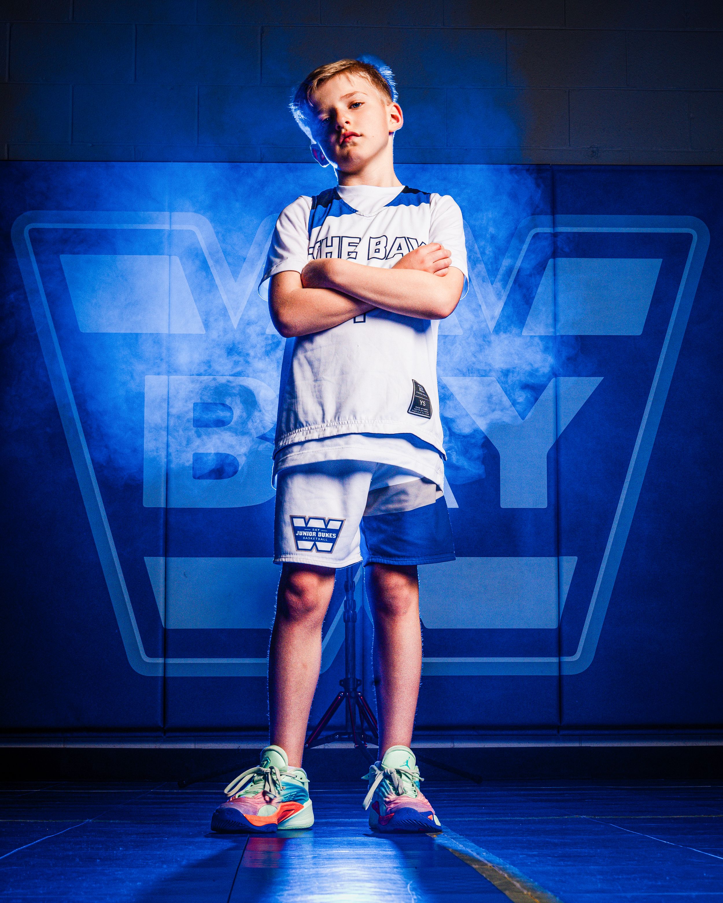 An athlete in white shorts and t-shirt strikes a confident pose against a dramatic blue-lit backdrop with bright sneakers.