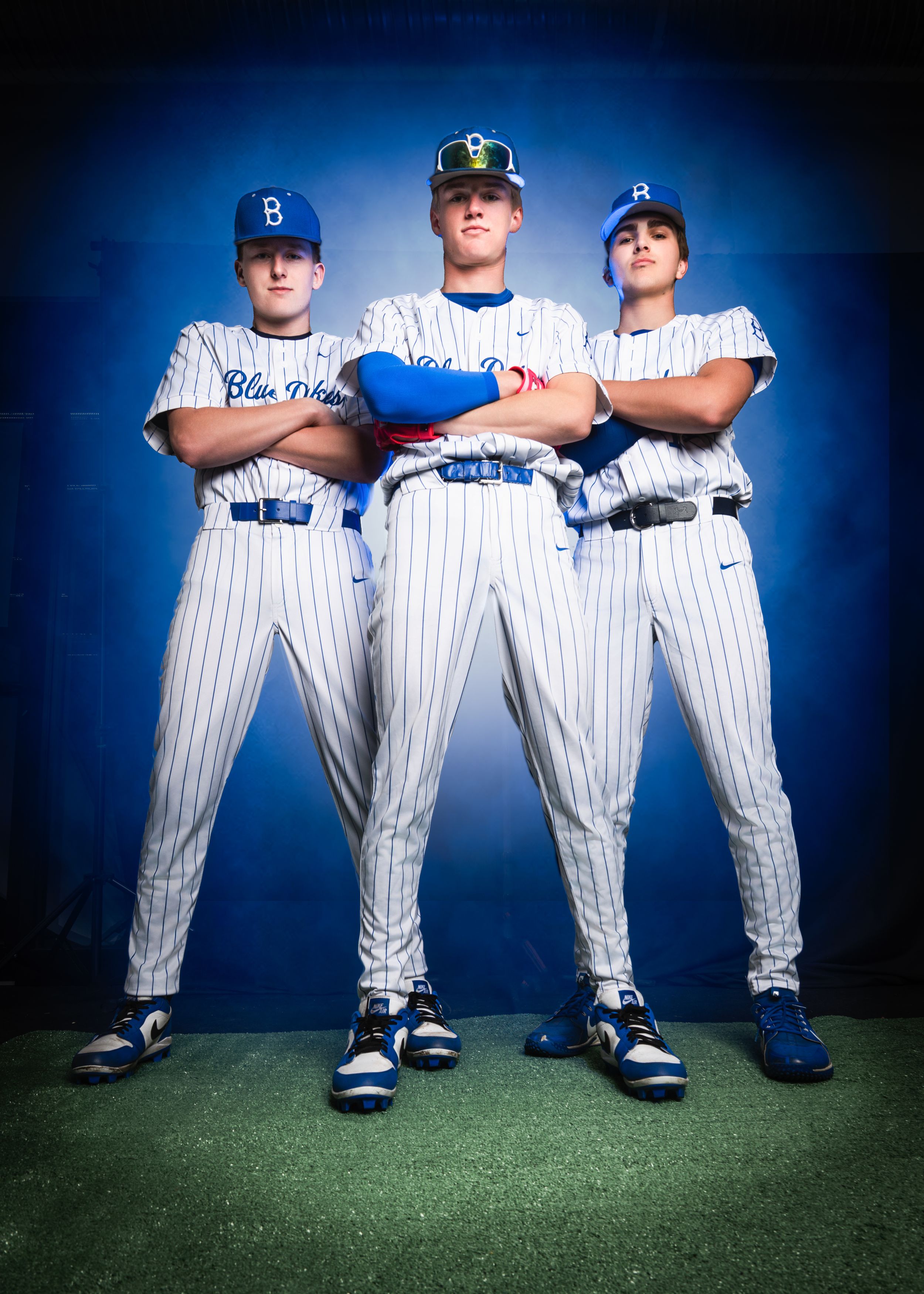 Baseball players in white pinstriped uniforms stand together in dramatic blue studio lighting, photographed from ground level.