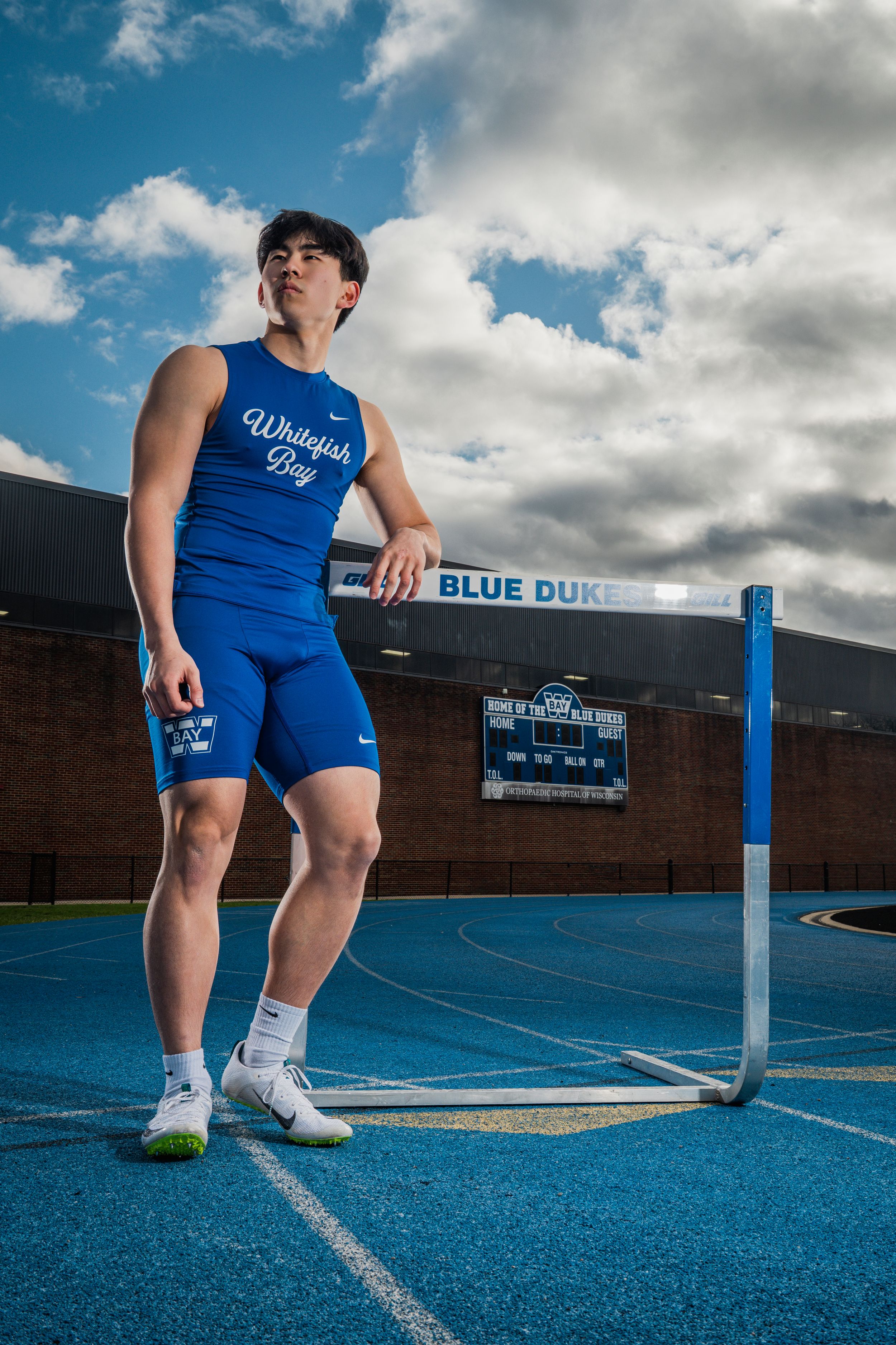 A person in blue workout attire is photographed from different angles on a blue track field with cloudy skies above.