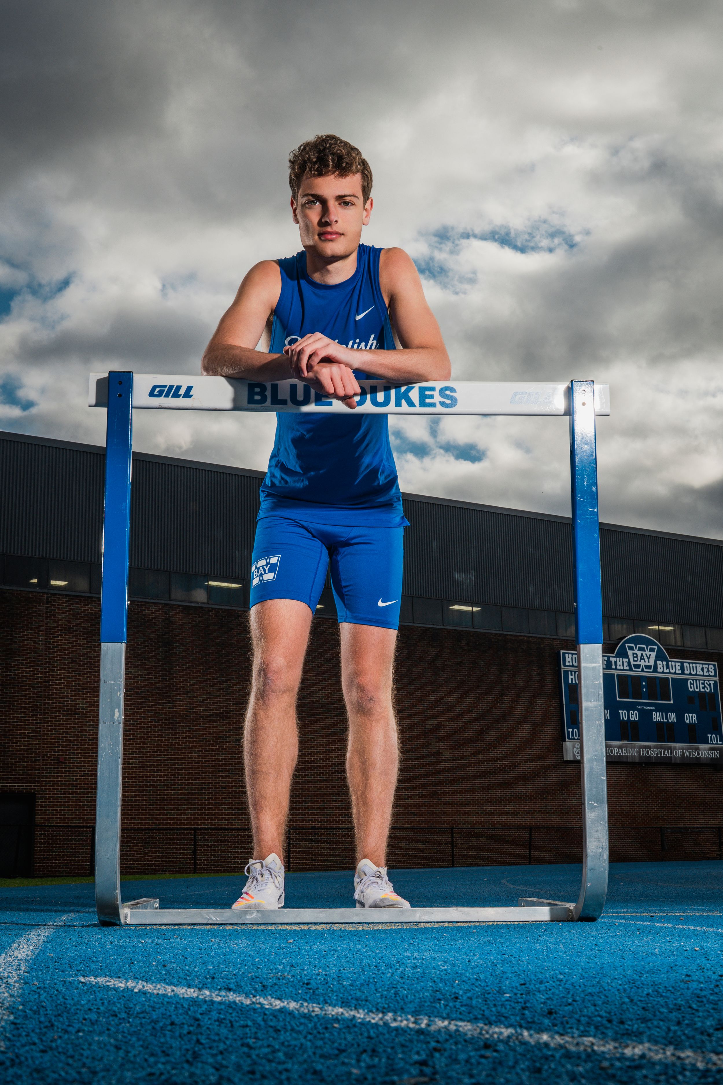 Training shot of athlete positioned at hurdle on outdoor blue running track.