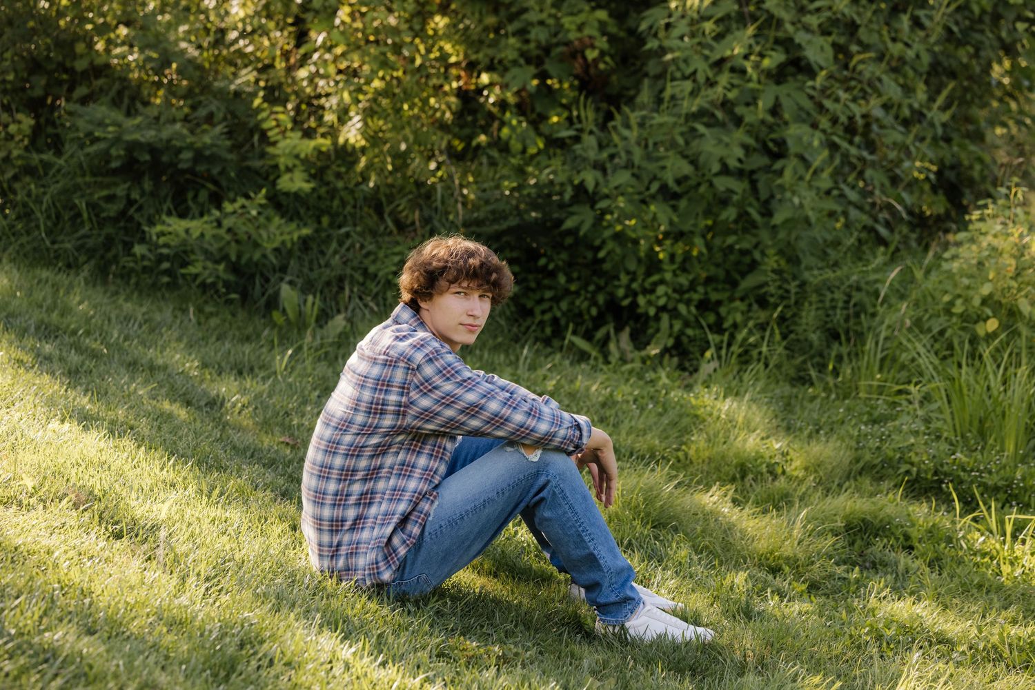 Laid-back portrait on grassy hillside wearing casual plaid and denim.