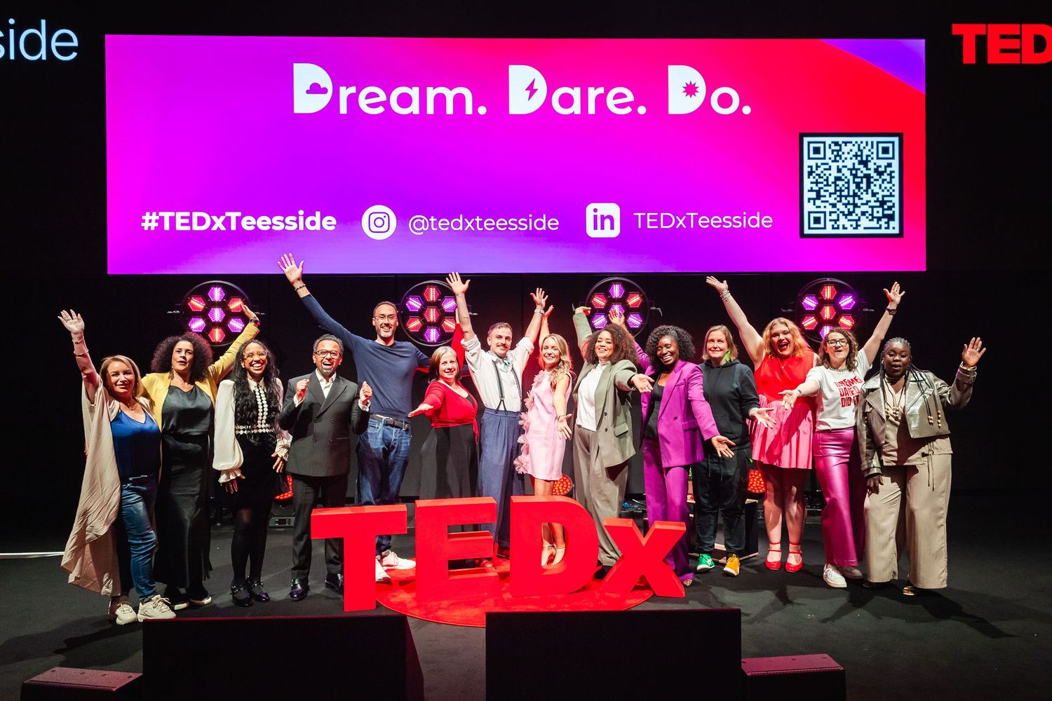 Performer in pink outfit on stage with TEDx letters and dramatic lighting.