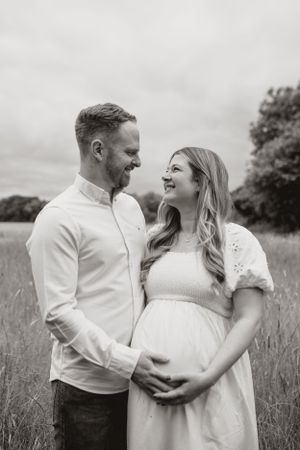 A couple shares a loving moment in a wildflower field during a maternity photo session in black and white.