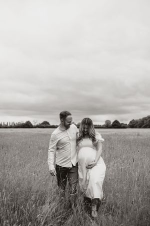 Romantic couple shares an intimate moment while walking through a tall grass field under moody cloudy skies.