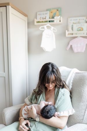 A tender moment of bonding and feeding in a cozy nursery chair beside a bright window.