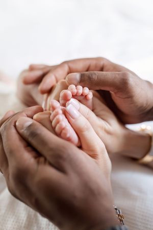 Adult hands gently hold and caress tiny newborn baby feet in a tender moment of connection.