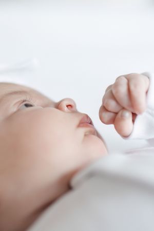 A sleeping baby lies peacefully on white bedding with a tiny fist raised near their face.