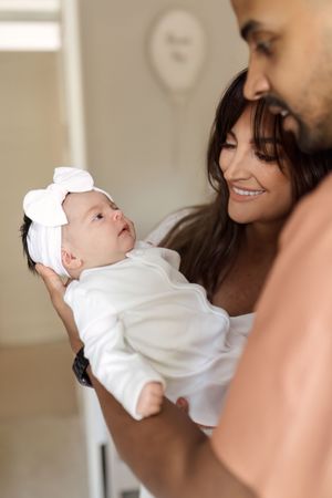 Parents share an intimate moment with their newborn baby dressed in white against a soft neutral background.