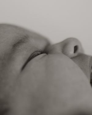 Close-up black and white portrait of a baby's facial features in soft focus, showing nose and closed eyes.