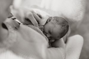 Tender black and white photo of newborn baby breastfeeding against soft fabric background.