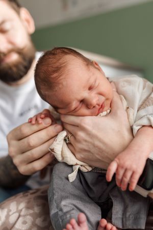 A sleeping newborn baby in gray clothing is cradled gently in someone's arms.