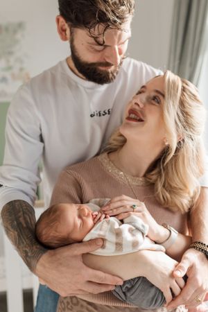 A joyful couple share a tender moment while holding their newborn baby in a naturally lit room.