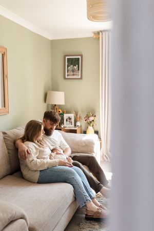 A couple relaxes together on a cozy gray couch in a softly lit living room with sage green walls.
