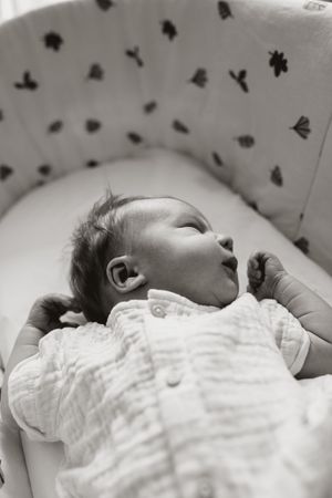 A sleeping baby in a white onesie lies peacefully against a patterned background in black and white.