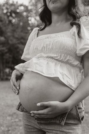 Black and white close-up photos showing a pregnant belly in a white ruffled top and jeans.