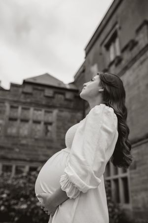 Black and white maternity portraits showing a woman in white dress against stone building backdrop.