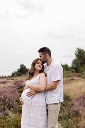 Romantic couple embraces in a field of purple heather during a sunset maternity photoshoot.