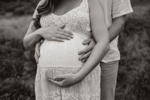A series of black and white maternity photos showing a pregnant belly in a white lace dress with hands tenderly embracing it.