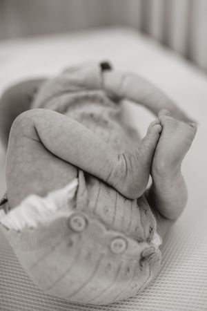 Close-up black and white photo of tiny baby feet curled up against soft fabric in crib.