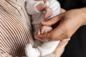 Close up of adult hands gently holding a tiny newborn baby's hand in soft, gentle lighting.