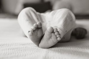Tiny baby feet in white socks rest on soft cotton bedding in black and white.
